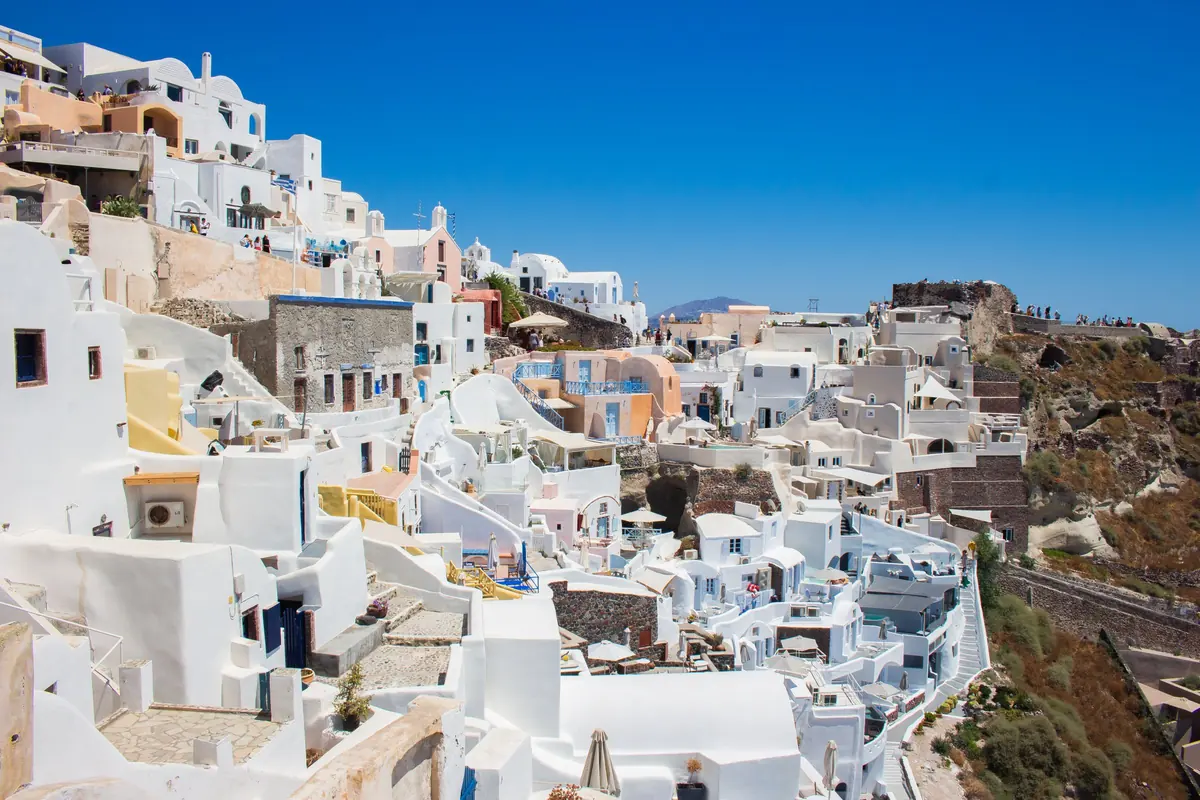 Bílené domy stupňovitě klesající po strmém svahu nad mořem na Santorini pod jasně modrou oblohou.